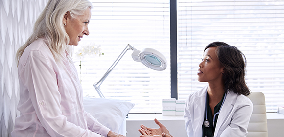 Older woman talking with young doctor about symptoms of bowel cancer.