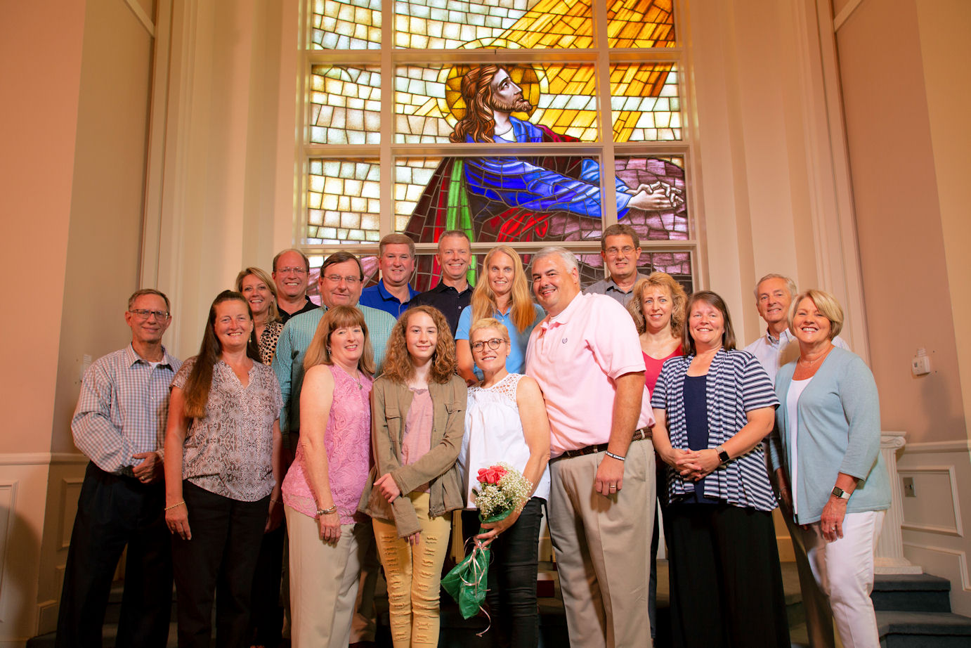 Large group of people surround Kimberly in front of stained glass window.